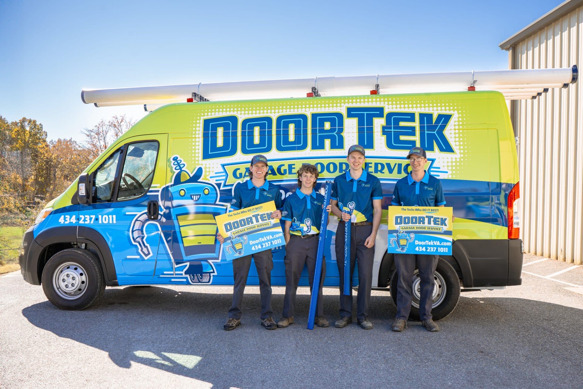 DoorTek team in their polos holding yard signs in front of their branded vehicle